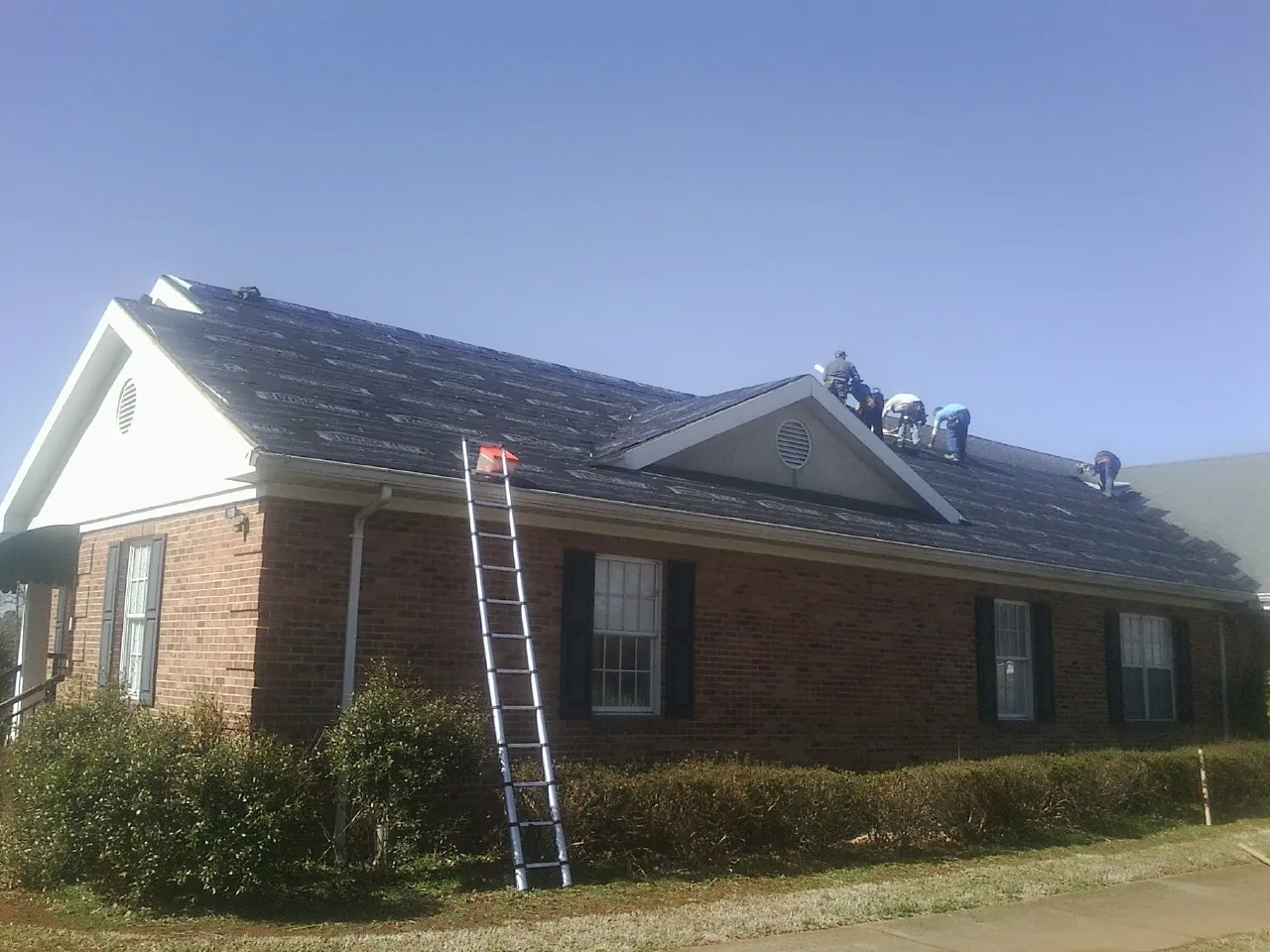 Crew tearing shingles off a brick ranch roof with a ladder set — Emergency Roof Repair work by our crew in Battle Mountain