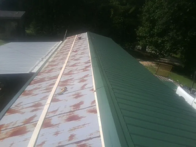 Old rusted panels beside newly installed green metal roofing — Wind Damage Roof Repair by Roofing Brothers in Battle Mountain