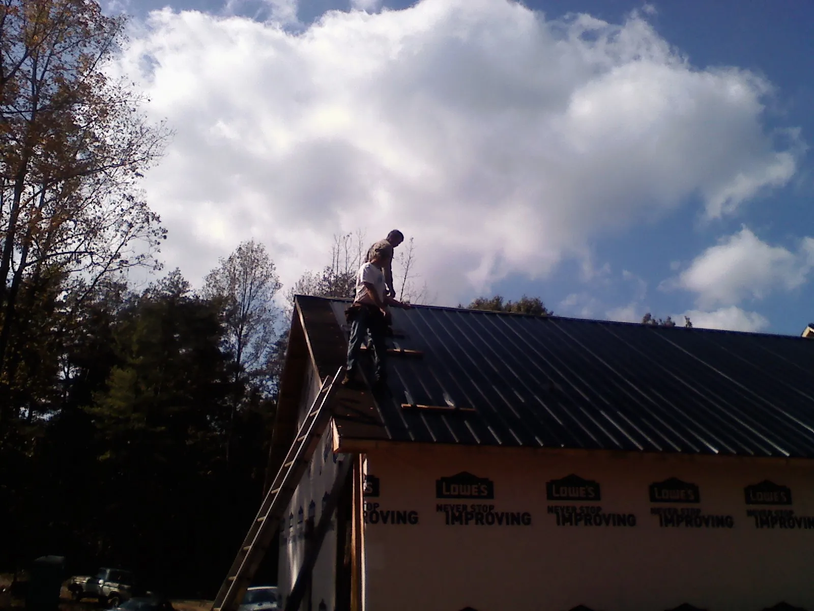 Roofer fastening dark metal panels high against a cloudy sky, from a Roof Inspection job in Battle Mountain